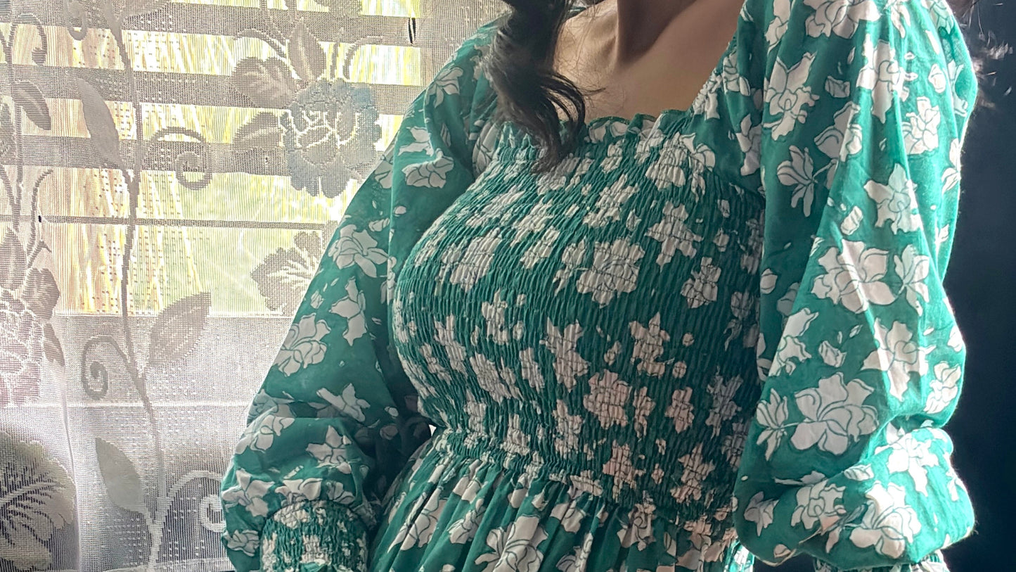 Person wearing a green summer floral dress sitting at a table with a window in the background