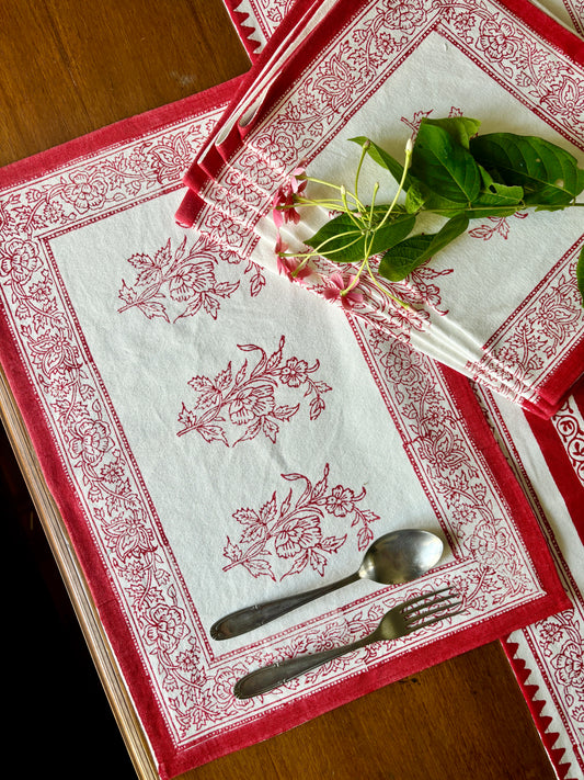 A set of red floral and geometric patterned dining placemats displayed on a table with a small floral arrangement in the center.