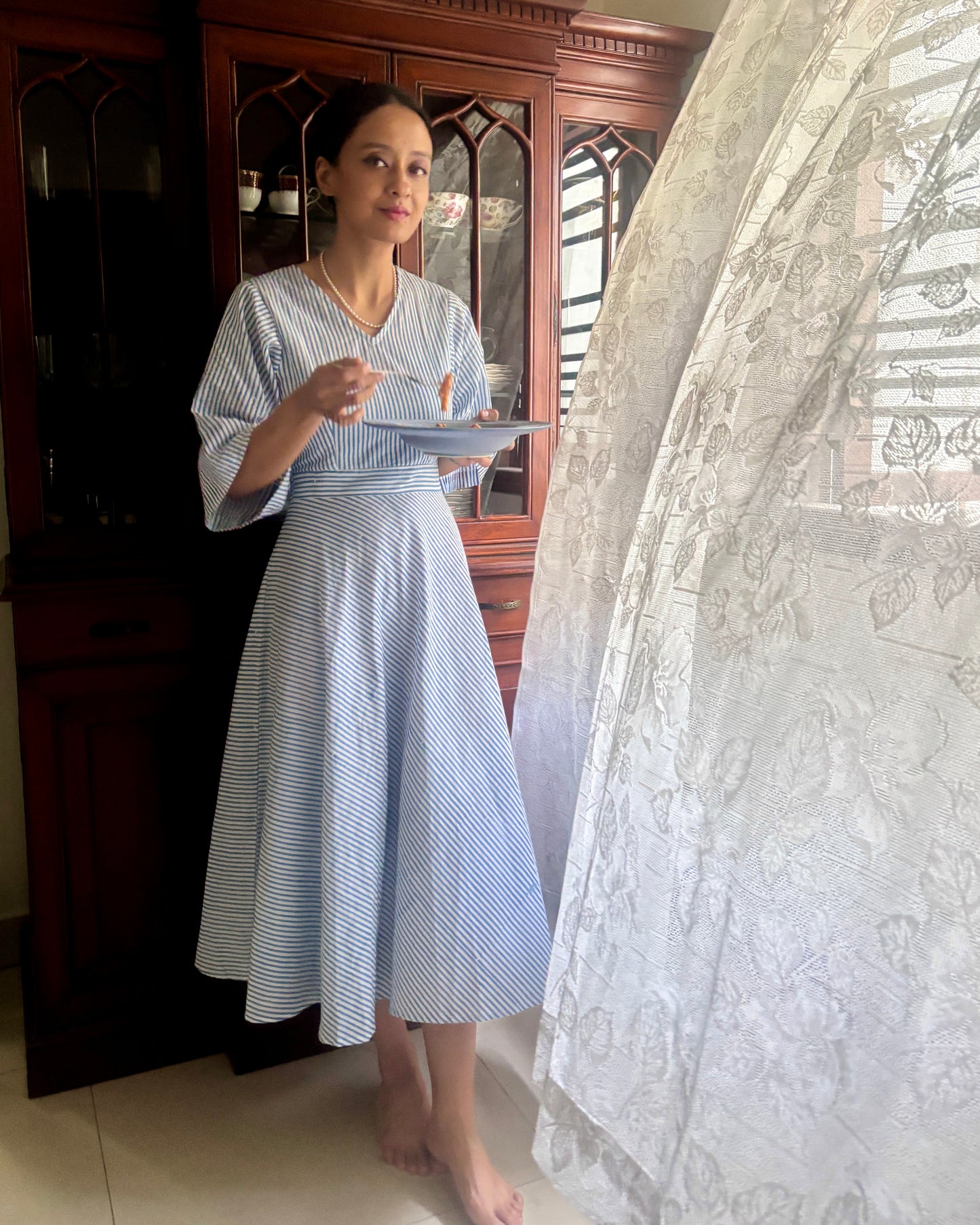 Woman in a blue and white striped dress that is vintage inspired and has retro charm. Shop this dress for garden parties and hosting brunches.